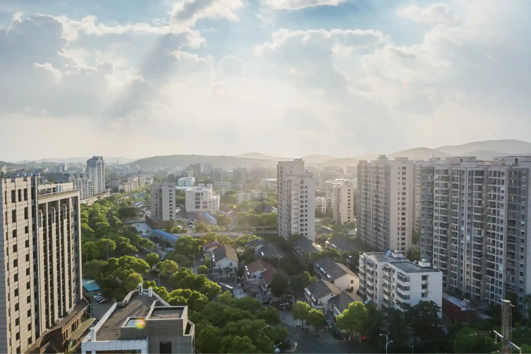 Aerial view of mid-rise residential buildings and tree-lined streets in an Indian city at soft morning light